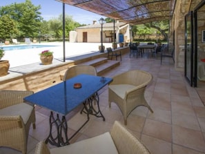 Eine überdachte Terrasse im Freien mit Pool, Korbmöbeln und Blick auf den Pool.