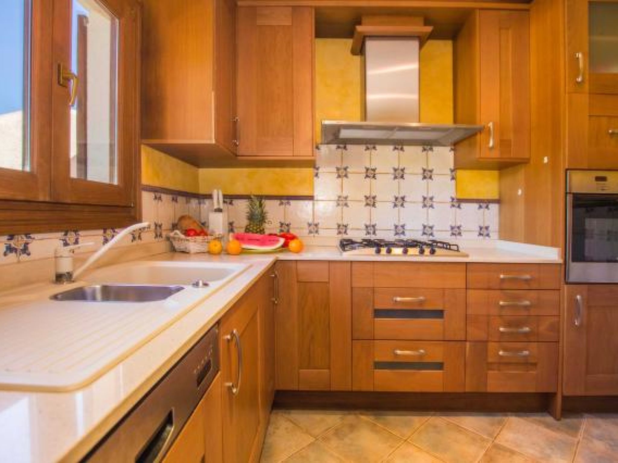 Une cuisine avec des meubles en bois, une cuisinière à gaz, un évier et un dosseret carrelé.