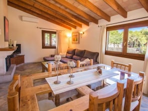 Ein gemütliches Wohnzimmer mit einem Holztisch und Stühlen, einem Sofa und einem Fenster mit Blick ins Grüne.
