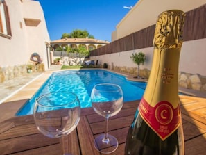 Eine Flasche Brut Nature Champagner, zwei leere Gläser und ein Swimmingpool mit Blick auf ein Gebäude.