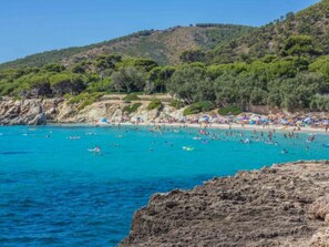 Ein Küstenstrand mit felsigen Klippen, klarem, blauem Wasser und Menschen, die schwimmen und sonnenbaden.