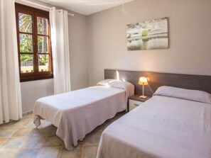 Una camera d'albergo con due letti, un comodino con una lampada, una finestra con tende e un quadro appeso al muro.