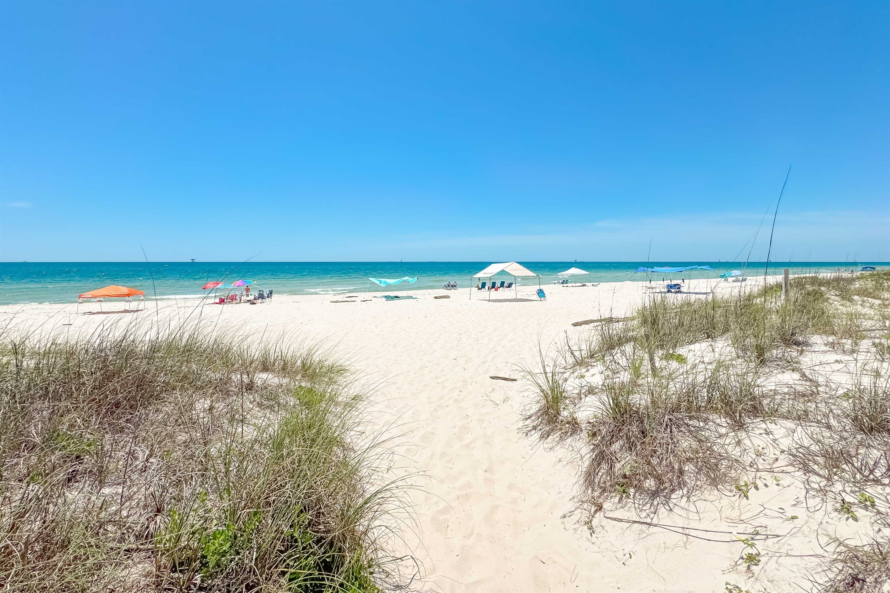 A beach with a clear path leading to the water, umbrellas, and beach chairs.