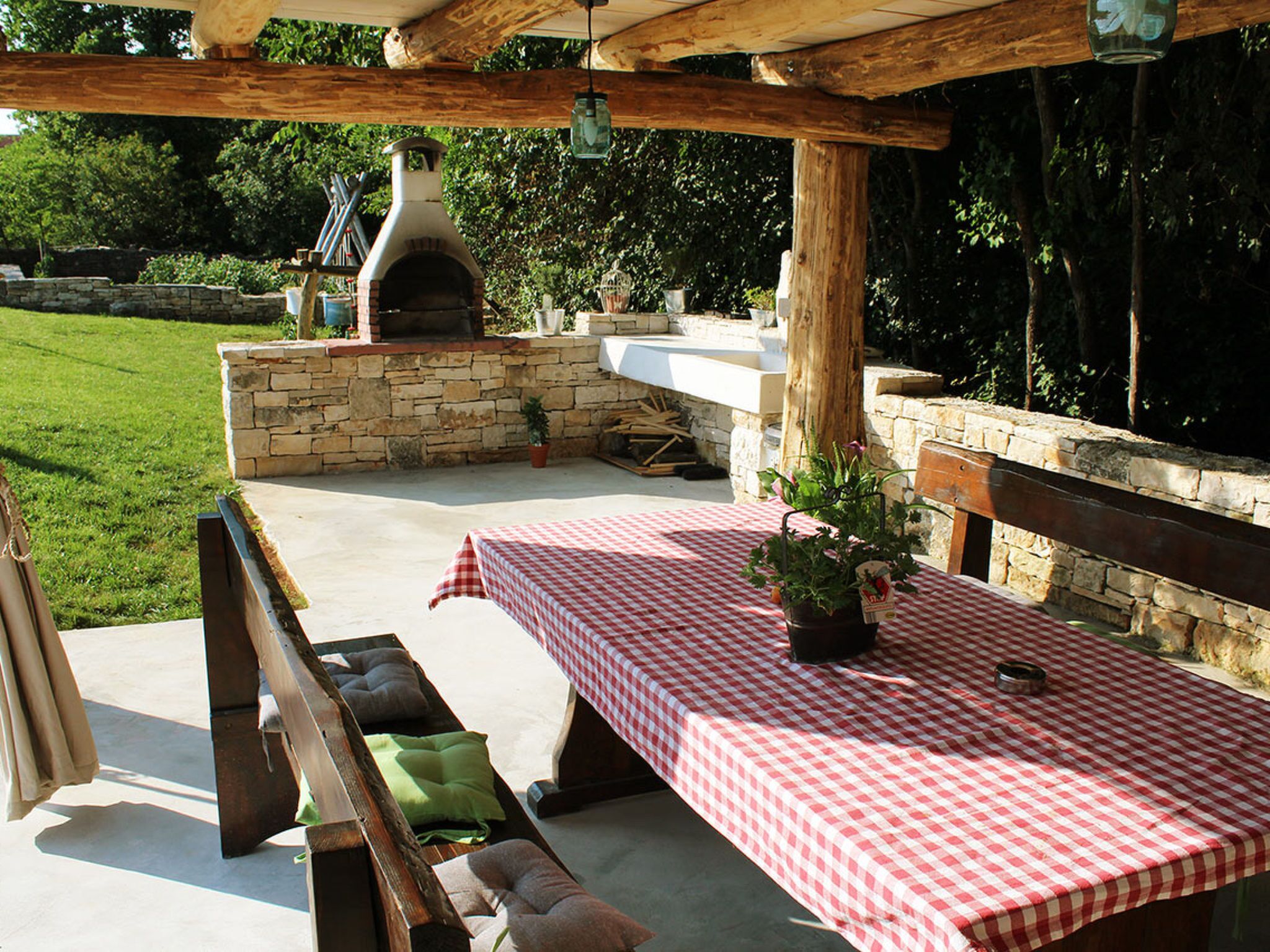An outdoor patio with a checkered tablecloth, stone walls, a wooden bench, and a stone fireplace.