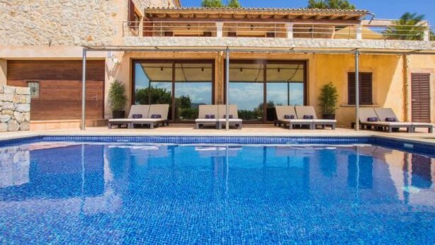 Un espace moderne aménagé au bord de la piscine, avec une piscine à l’eau d’un bleu limpide, des chaises longues et une façade en pierre.