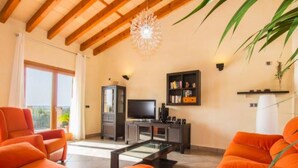 Uma sala de estar com sofás laranja, uma TV, uma estante e um ventilador de teto.