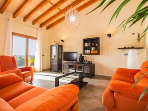 Ein Wohnzimmer mit orangenen Sofas, einem Fernseher, einem Bücherregal und einem Deckenventilator.