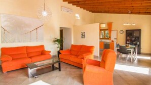 Uma sala de estar ampla com sofás laranja, uma mesa de centro de vidro e teto de madeira.