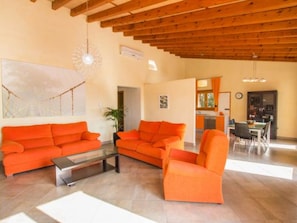 Ein geräumiges Wohnzimmer mit orangefarbenen Sofas, einem Glastisch und einer Holzbalkendecke.