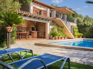 Eine zweistöckige Villa mit Pool, Sitzgelegenheiten im Freien und einer Treppe, die zum Obergeschoss führt.