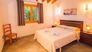 Quarto com cama, poltrona, janela com cortinas, um quadro na parede e duas luminárias de cabeceira.