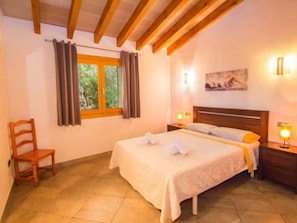 Ein Schlafzimmer mit einem Bett, einem Sessel, einem Fenster mit Vorhängen, einem Bild an der Wand und zwei Nachttischlampen.