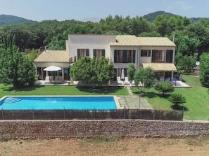 Ein zweistöckiges Haus mit Schwimmbad, umgeben von Grün und Hügeln.