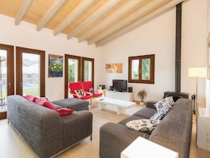 Ein geräumiges Wohnzimmer mit hohen Decken, großen Fenstern, einem Kamin und einem Fernseher.