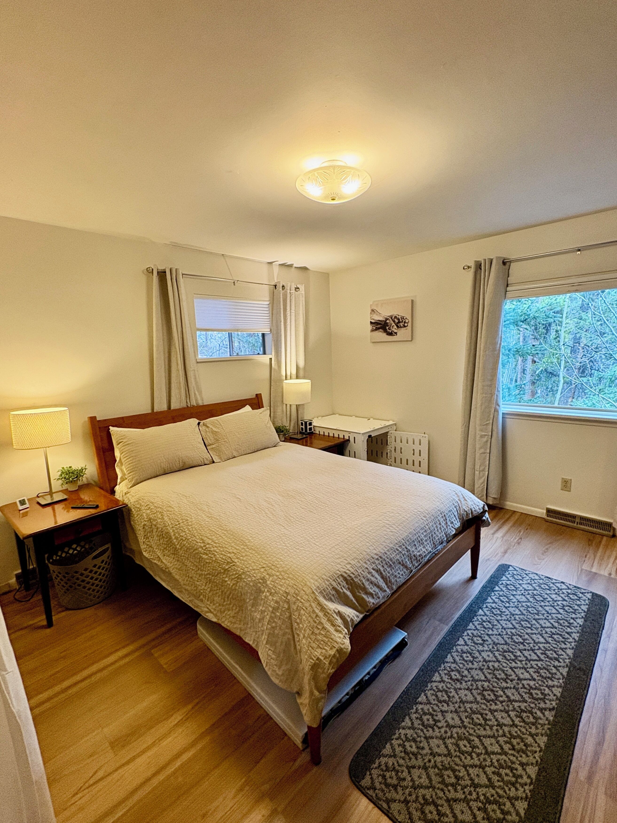 Un dormitorio con cama, mesitas de noche, una lámpara, un radiador y una ventana con cortinas.