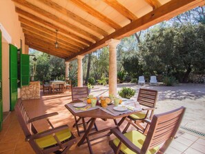 Eine überdachte Terrasse mit Tisch für zwei Personen, umgeben von Stühlen mit Kissen.