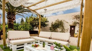 A covered outdoor seating area with white sofas and a coffee table, surrounded by greenery and a clear sky. - Manyo Petit by Interhome (Sa Pobla)