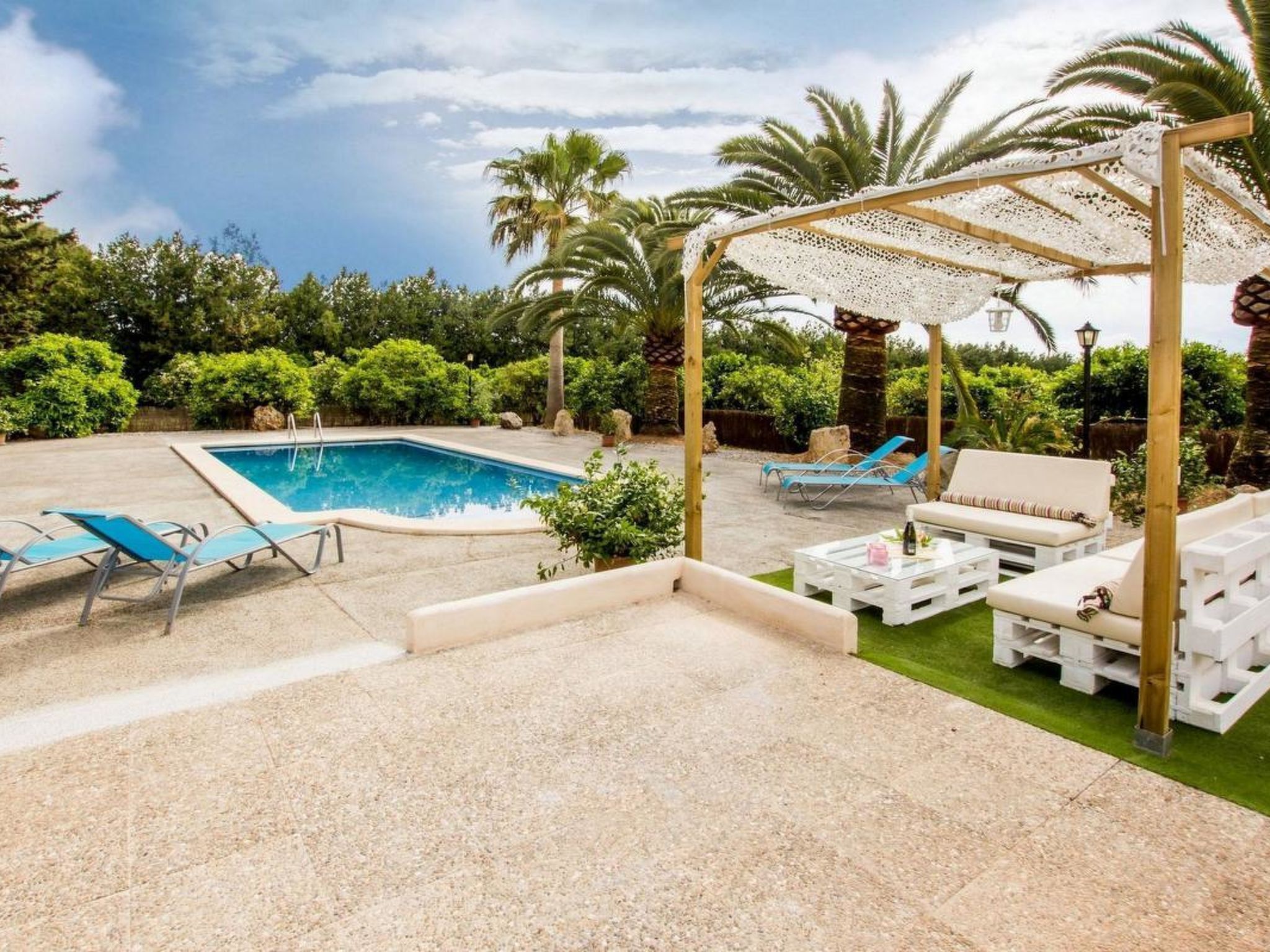 A pool area with a pergola, lounge chairs, and a white outdoor sofa.