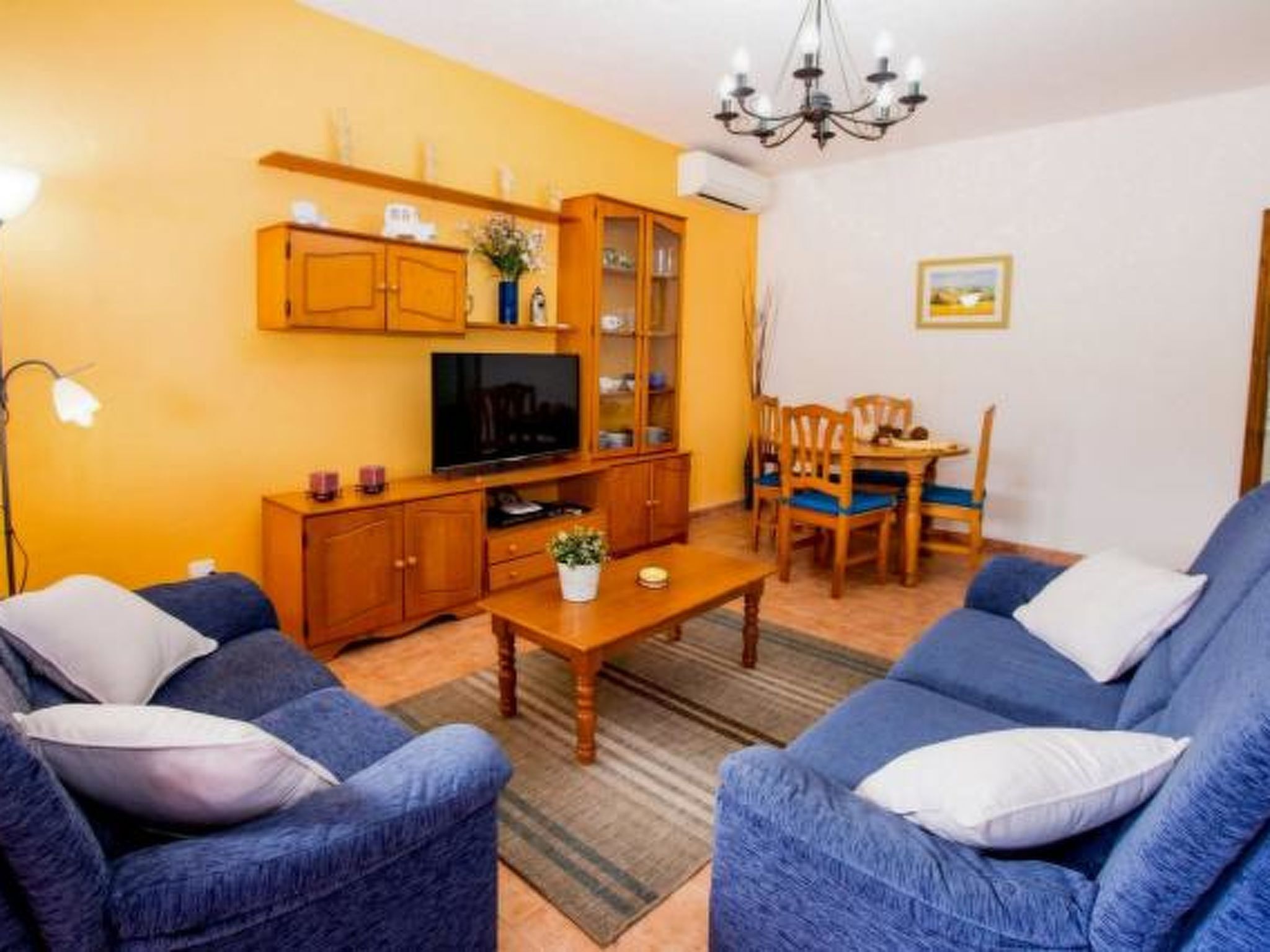 A living room with a sofa, TV, wooden cabinets, and a dining area with chairs.