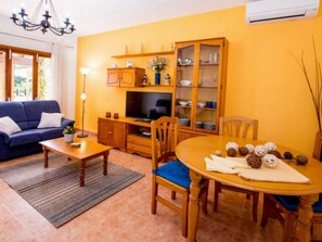 Ein Wohnzimmer mit Sofa, Fernseher, Holzschrank, Esstisch mit Stühlen und einer Chandelier.