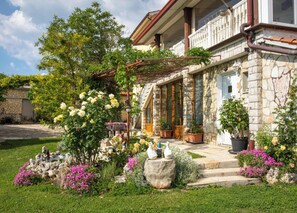 Een stenen gebouw met een balkon, omringd door een verzorgde tuin met diverse planten en bloemen.