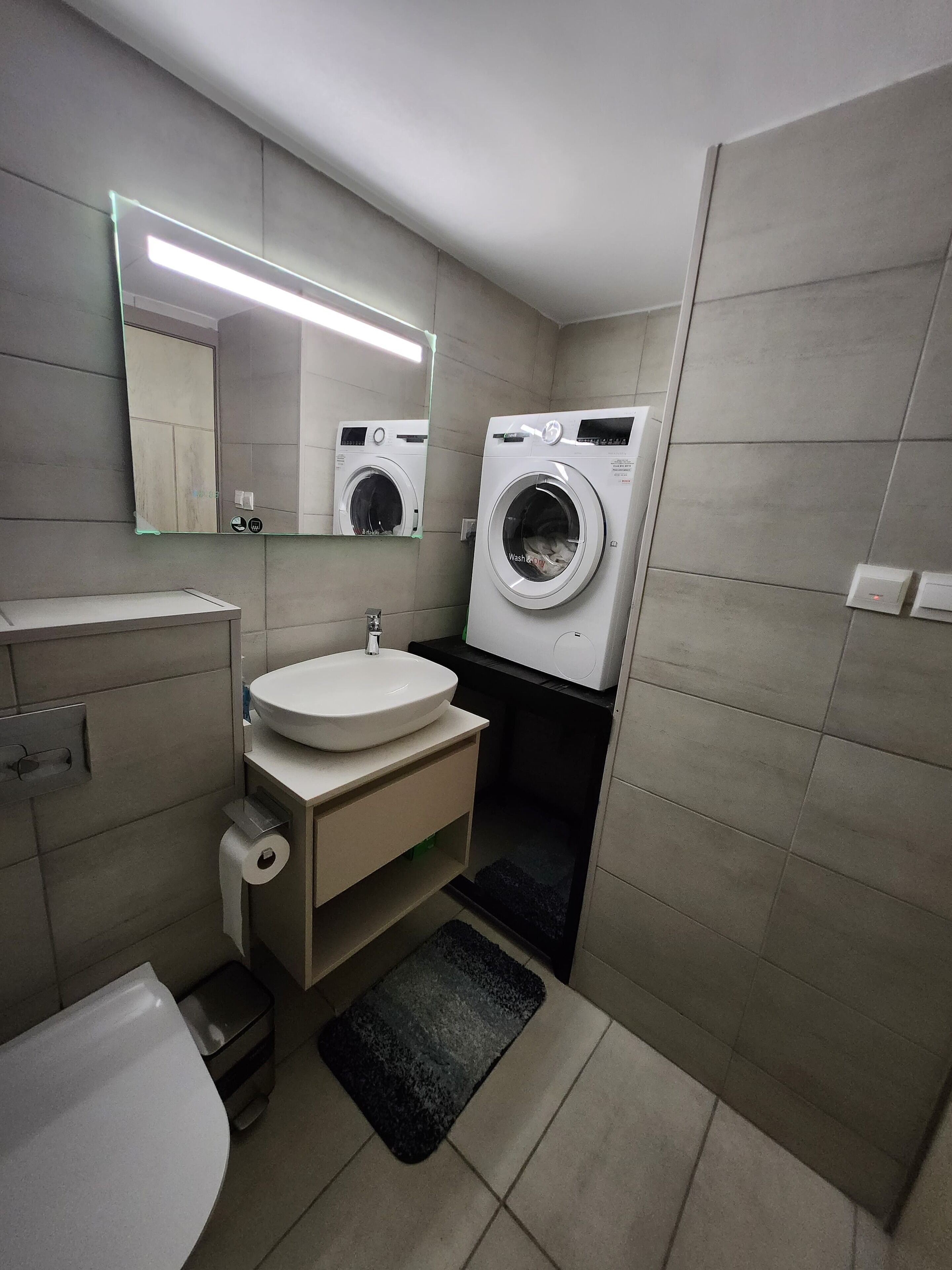 Un baño moderno con lavamanos, espejo, inodoro y lavadora.