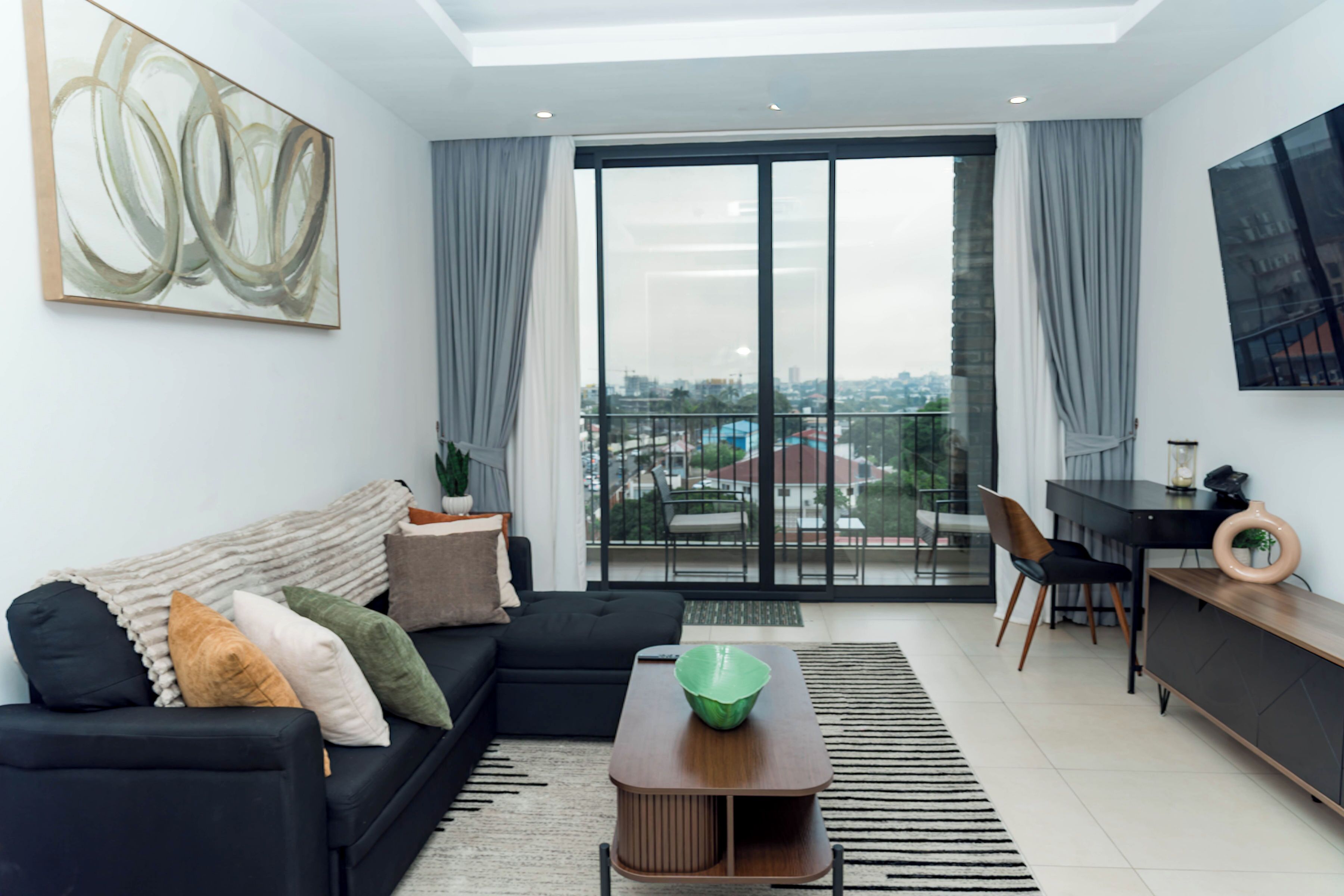 A modern living room with a black sofa, a coffee table, and a view through a large glass door.