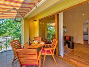 A balcony with a striped awning, a wooden table, and chairs. - Irena Apartments 2 kat / HR-10649-02 by Interhome (Selce)