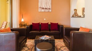 A living room with a brown leather sofa, red cushions, a coffee table with magazines, and a painting of sailboats on the wall. - Irena Apartments 2 kat / HR-10649-02 by Interhome (Selce)