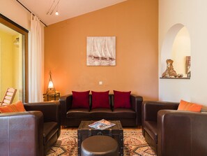 A living room with a brown leather sofa, red cushions, a coffee table with magazines, and a painting of sailboats on the wall. - Irena Apartments 2 kat / HR-10649-02 by Interhome (Selce)