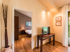 Une chambre d’hôtel avec un plancher en bois, un lit, un téléviseur posé sur un meuble en bois et un tableau accroché au mur.