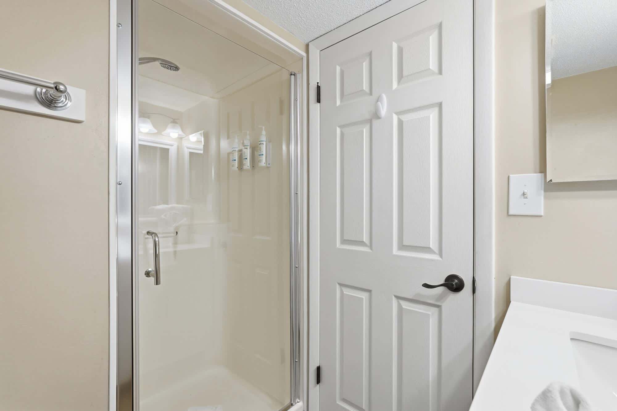 Une salle de bain avec une porte blanche, un espace douche et un miroir au mur.