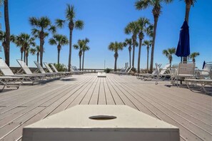 A wooden deck with white lounge chairs and palm trees.