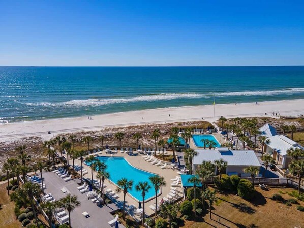 An aerial view of a resort with a swimming pool, beach access, and palm trees.