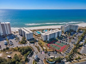 A beachfront hotel with multiple buildings, a parking lot, and a tennis court.