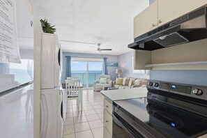 A modern kitchen with a stove, oven, and refrigerator. There is a dining area with a table and chairs. - The Summit 1421 - Wake to Gulf Views! Includes Seasonal Beach Chairs (Panama City Beach)