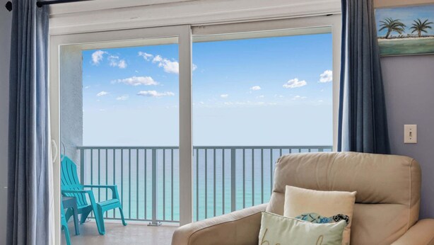 Una stanza con un divano color crema, una poltrona azzurra e vista sull'oceano tramite una porta scorrevole in vetro.