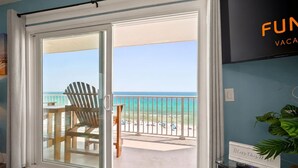 Ein Zimmer mit einer Schiebetür zu einem Balkon mit Blick auf Strand und Meer.