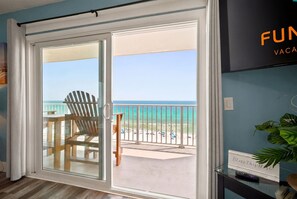 Ein Zimmer mit einer Schiebetür zu einem Balkon mit Blick auf Strand und Meer.