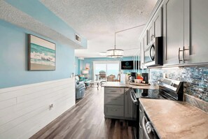 Eine moderne Küche mit einer großen Kochinsel, ein Essbereich mit Ausblick und ein Wohnzimmer mit Fernseher.