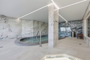 Ein moderner Wellnessbereich mit Whirlpool, Marmorwänden und einer Holzbank.