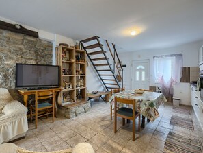 A cozy living room with a TV, wooden furniture, a bookshelf, a dining table with chairs, a staircase, and a kitchen area. - House Rea by Interhome (Buzet)