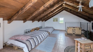 Een slaapkamer in loftstijl met een schuine balklaag, een bed met gestreepte beddengoed, een klein tafeltje en een raam.