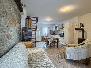 A cozy living room with a stone wall, a wooden ladder, a television, a sofa, and a dining area with chairs and a table. - House Rea by Interhome (Buzet)
