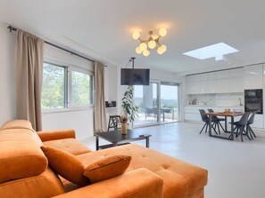 Een moderne woonkamer met een bank, een eethoek met stoelen, een tafel en een keuken met kasten en apparatuur.
