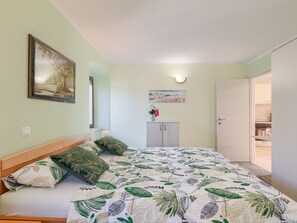 A bedroom with a bed, a nightstand, a cabinet, a painting, and a door leading to a kitchen. - House Horizon by Interhome (Pićan)