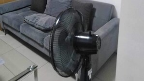 Un soggiorno con un divano grigio, una ventola a piantana, un armadio in legno e una TV a muro.