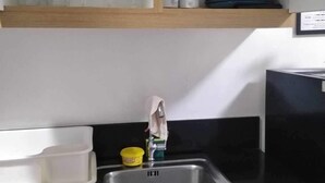 Una cucina con un lavandino in acciaio inossidabile, un pensile in legno e un piano di lavoro con un contenitore giallo e un espositore per piatti bianco.