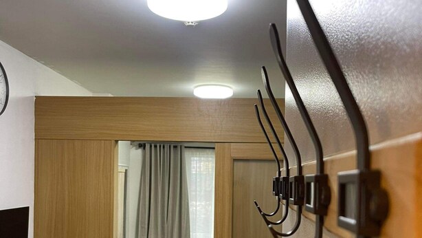 Camera d'albergo moderna con una porta in legno, zona pranzo con tavolo e sedie, un letto e una lampada a sospensione.
