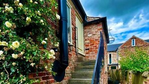 Un escalier étroit en pierre mène à un bâtiment en briques doté d’une rambarde en métal.